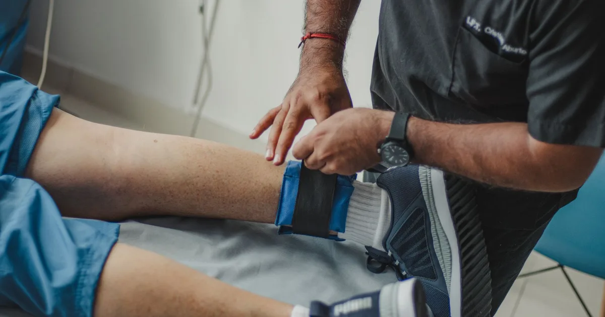 Fisioterapeuta ajustando uma cinta no tornozelo de um paciente deitado na maca
